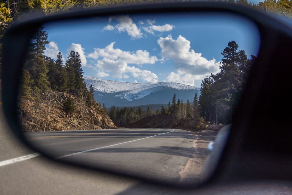 View of a scenic mountain highway in Canada reflected in a car side mirror during a road trip