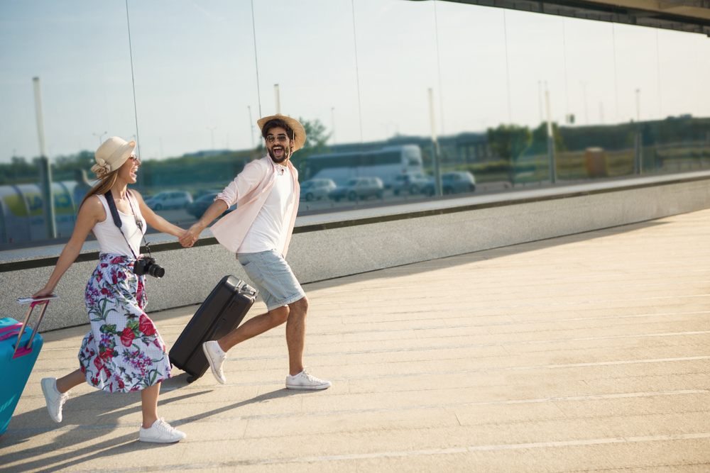 Excited young couple rushing with suitcases for a spontaneous summer trip, symbolizing last-minute travel freedom