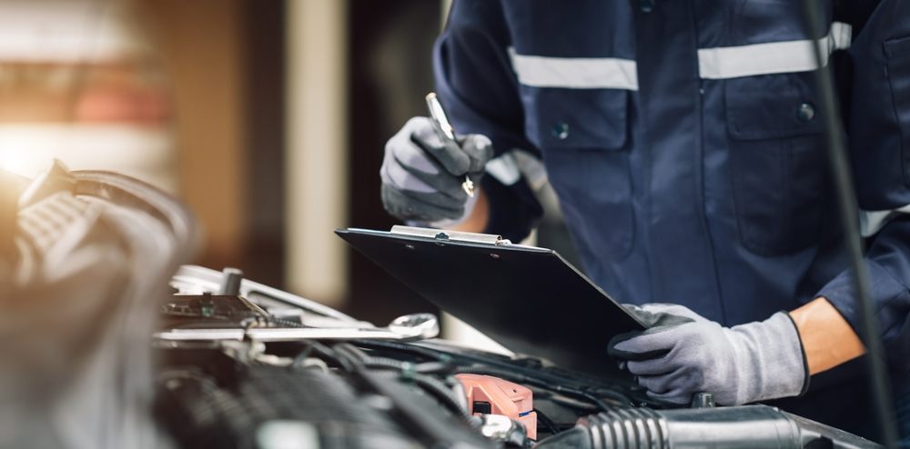 Auto mechanic inspecting engine and writing repair notes on clipboard before vacation travel