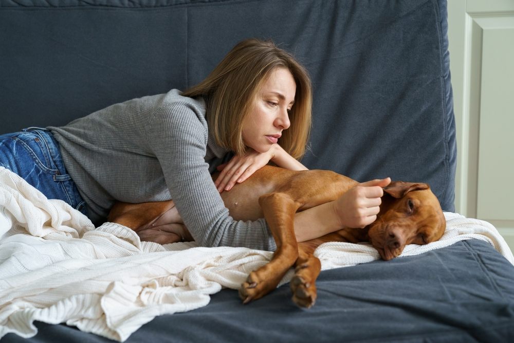 Concerned woman comforting her sick dog after an emergency vet visit, worried about paying the unexpected bill