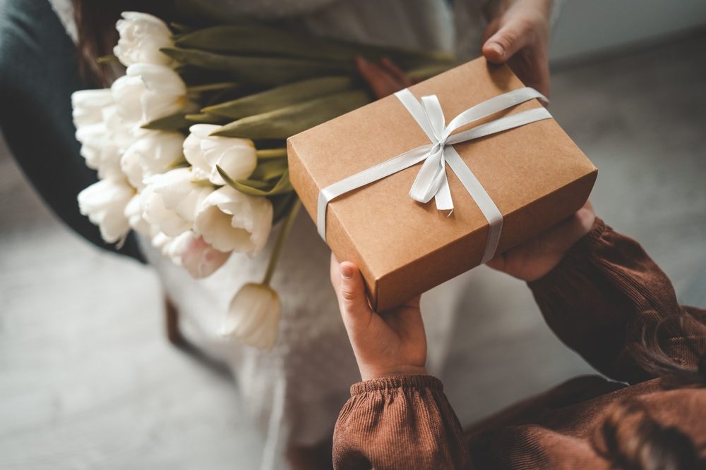 Hands exchanging a wrapped birthday gift and white tulip bouquet—perfect last-minute present thanks to a fast Loan Express loan
