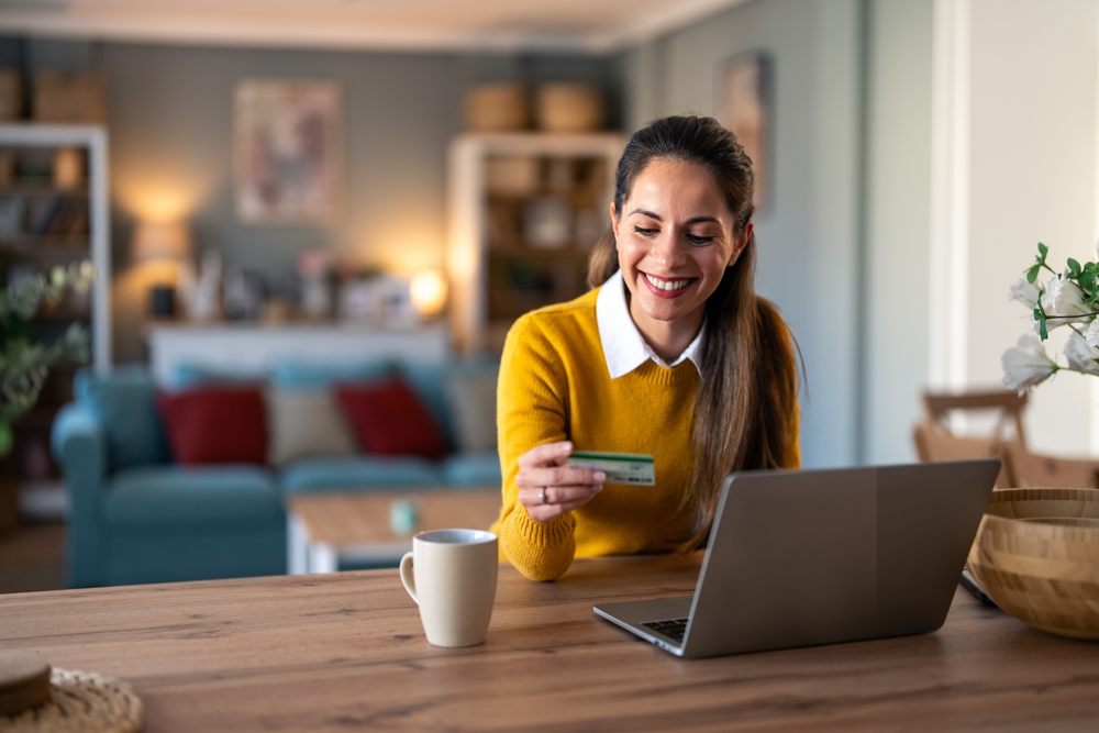 Smiling woman checking finances online with credit card and laptop — representing credit score vs credit report in Canada