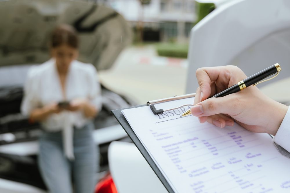 Insurance agent filling out a car insurance form while driver waits by a broken car – payday loan for renewal or deductible in Canada