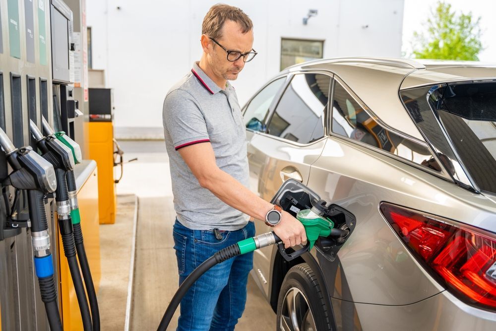 A man in a gray collared t-shirt filling gas up into a gold car, courtesy of a gas money loan.