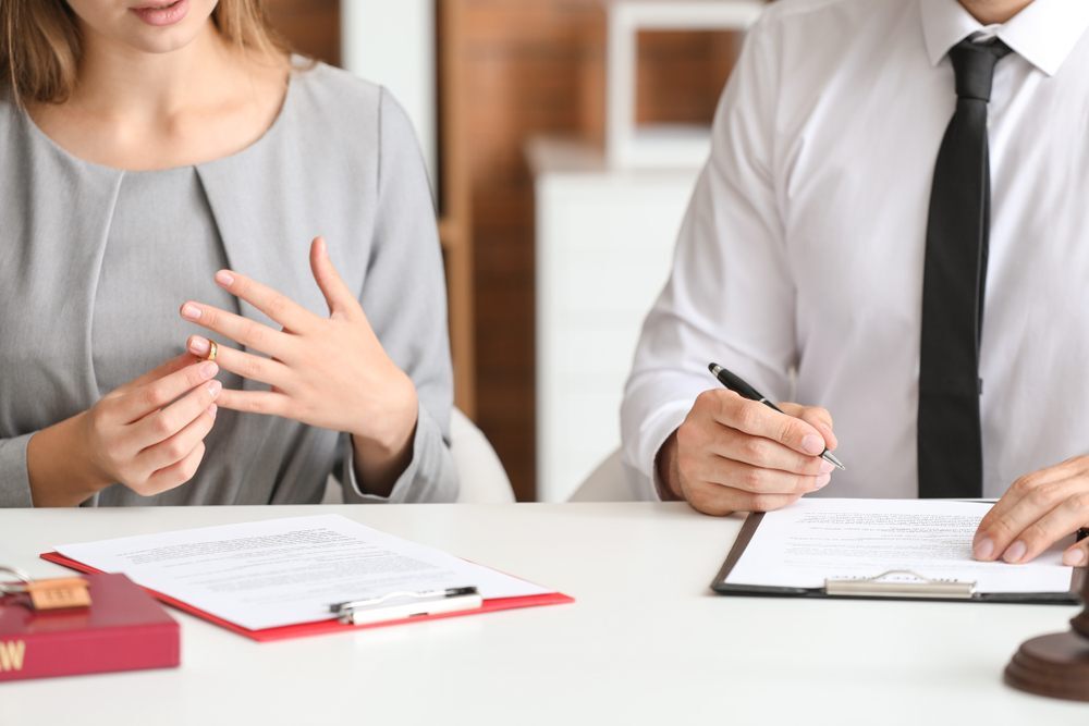 Woman removing wedding ring while reviewing divorce paperwork with a lawyer — financial stress and legal fees during separation in Canada