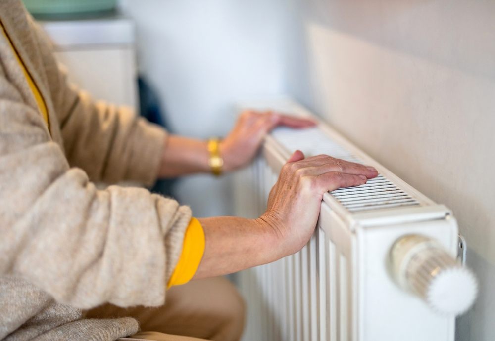 Person adjusting home heating radiator to manage winter utility costs and heating bills