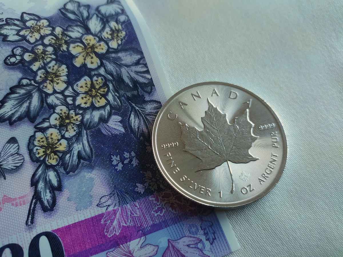Silver Canadian maple leaf coin resting on a Canadian banknote.