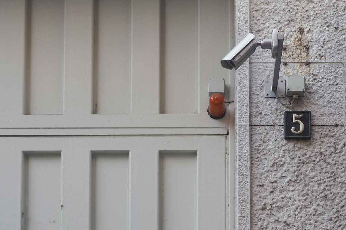 A home security camera next to a garage door on a white house.