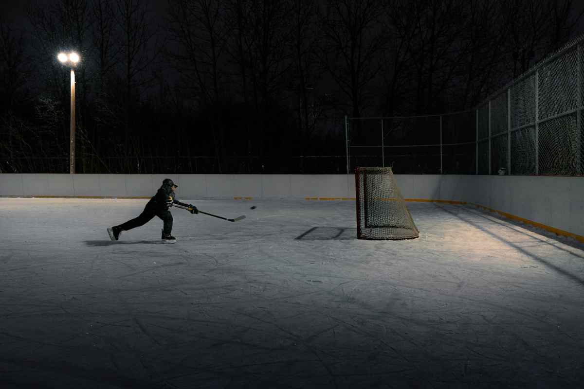 Person playing hockey alone on an outdoor rink at night.