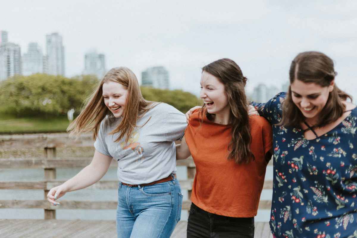 Three women laughing together outdoors with a city skyline in the background.
