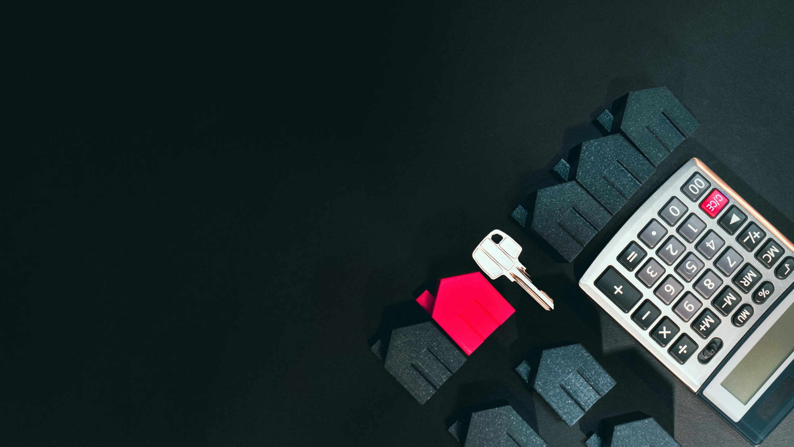 Real estate concept image featuring a calculator, houses, and a key on a black background