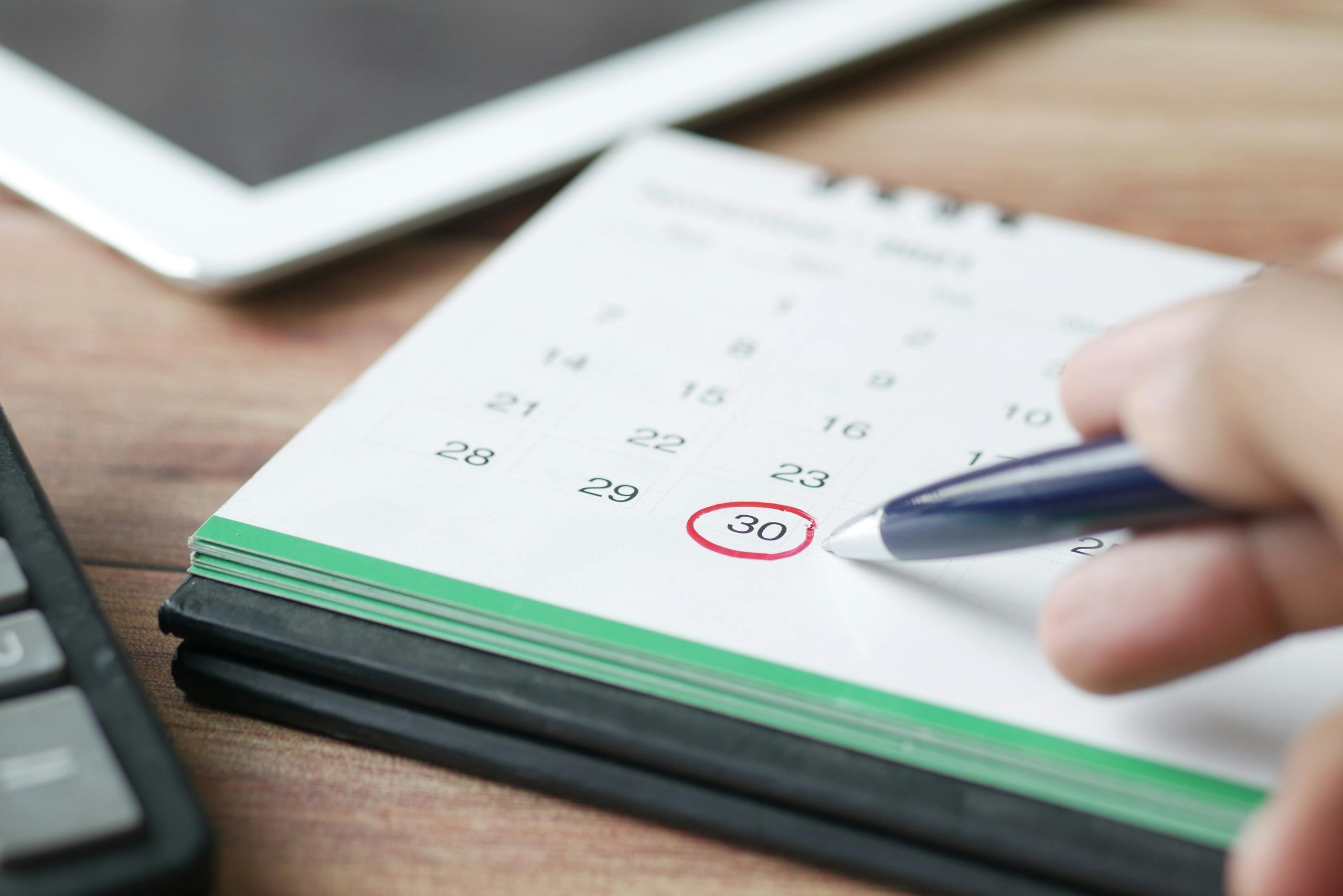 Close-up shot of a hand marking a date on a calendar with a pen, emphasizing planning and scheduling