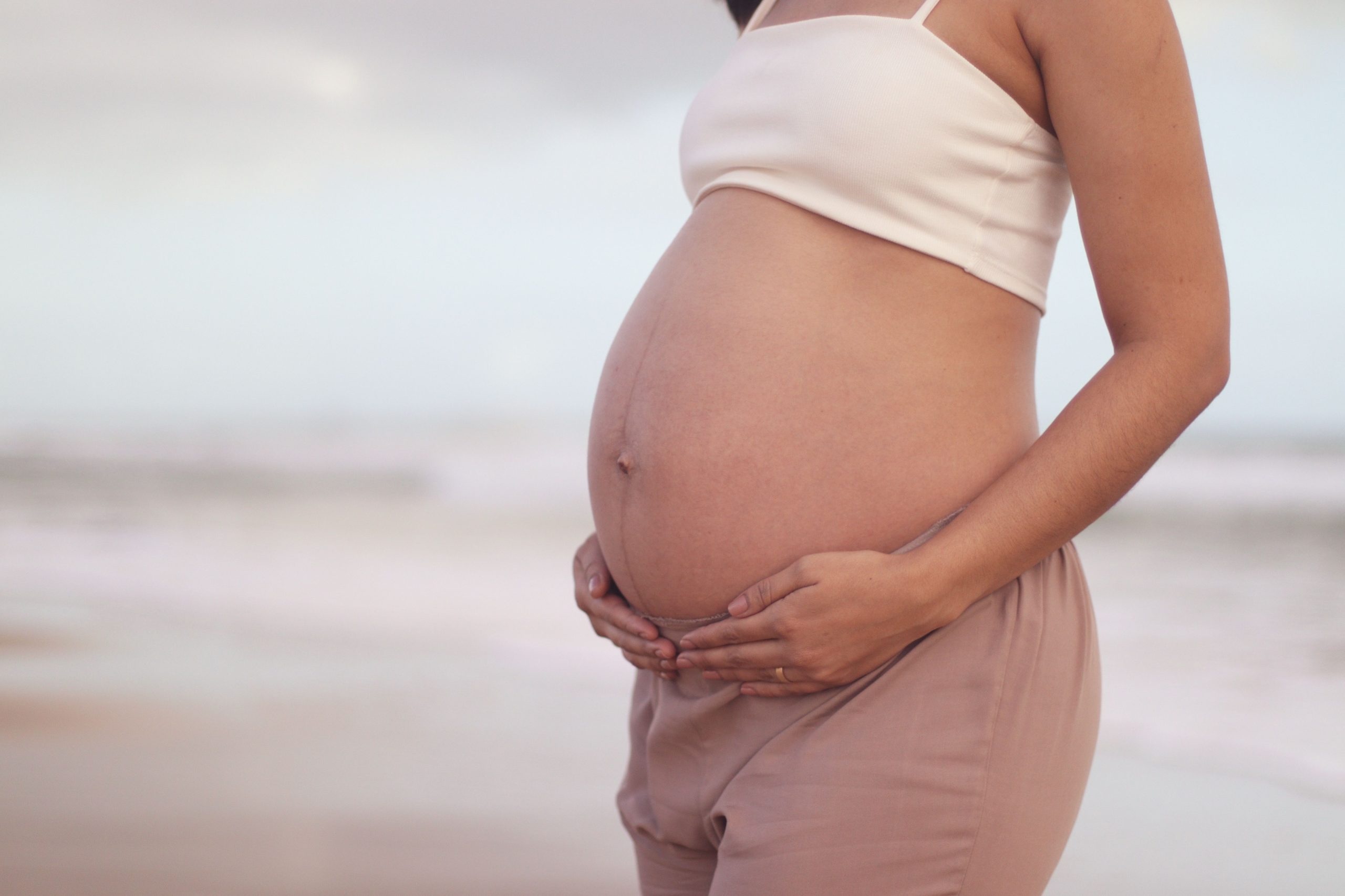 image of a pregnant woman cradling her belly on a tranquil beach