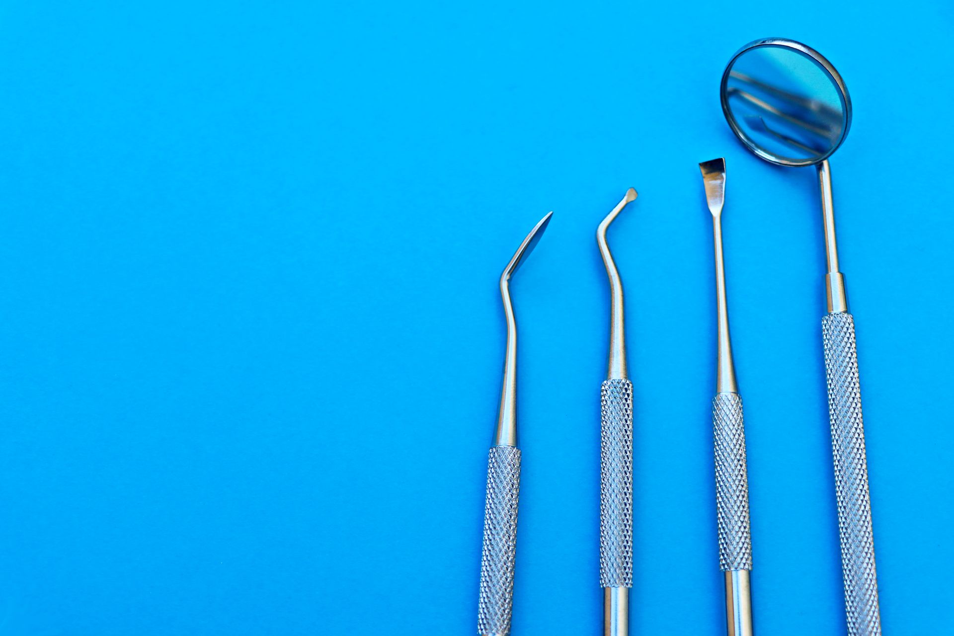 Close-up of stainless steel dental tools arranged on a bright blue surface, showcasing various instruments