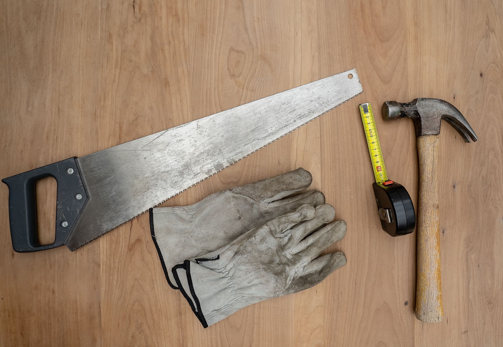 Flat lay of essential carpentry tools including a saw, hammer, and tape measure on a wooden surface.