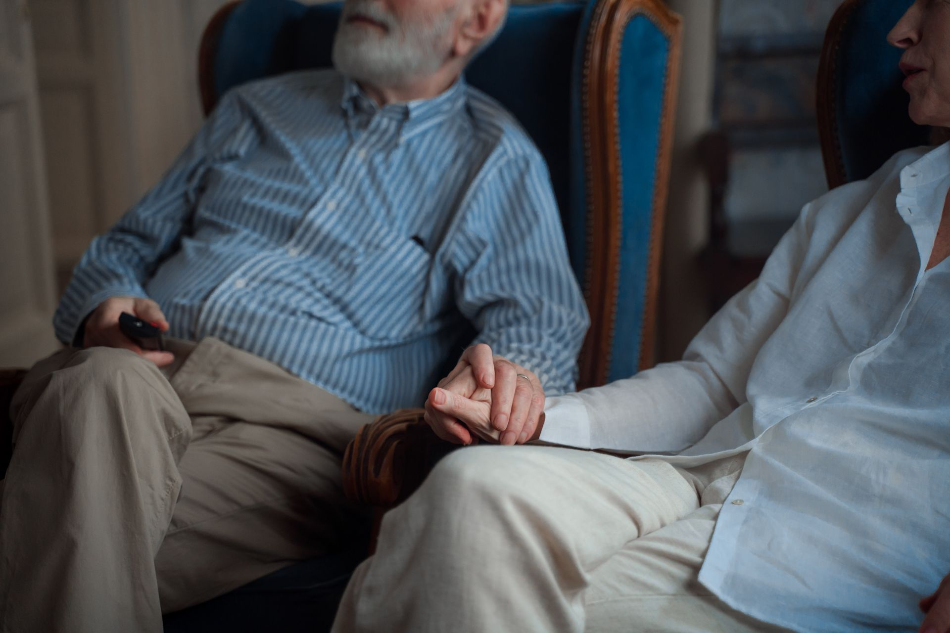 An elderly couple sitting together, holding hands in a cozy room, symbolizing companionship