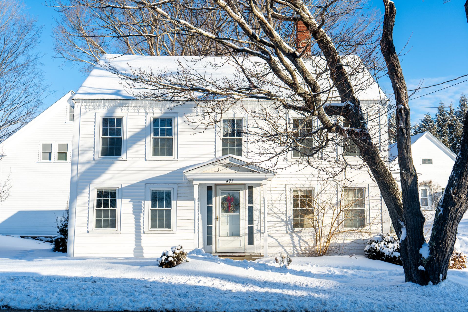 Beautiful colonial-style house covered in snow during a bright winter day, showcasing classic architecture.