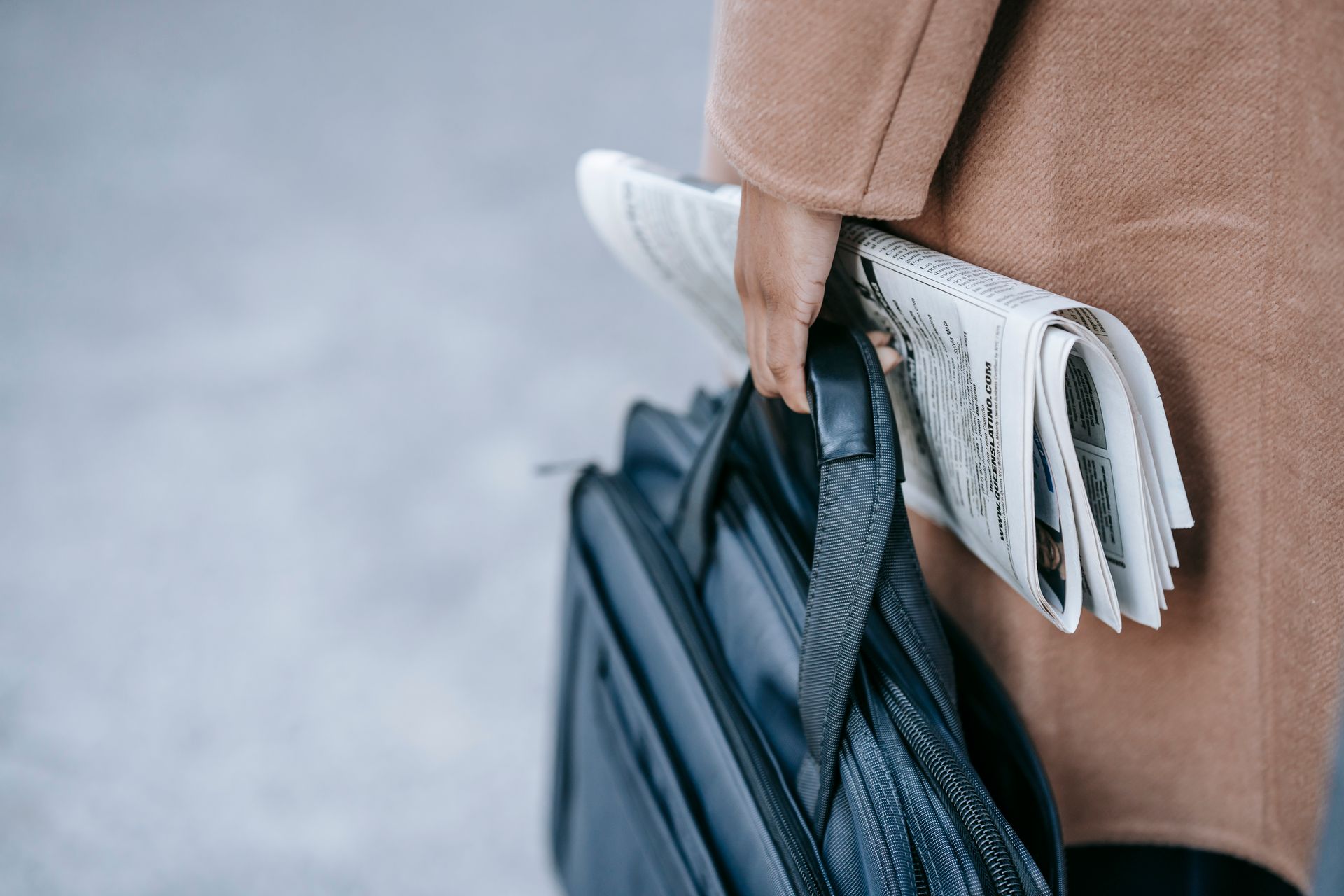 Close-up of a business professional holding a newspaper and briefcase, symbolizing work and information on the go