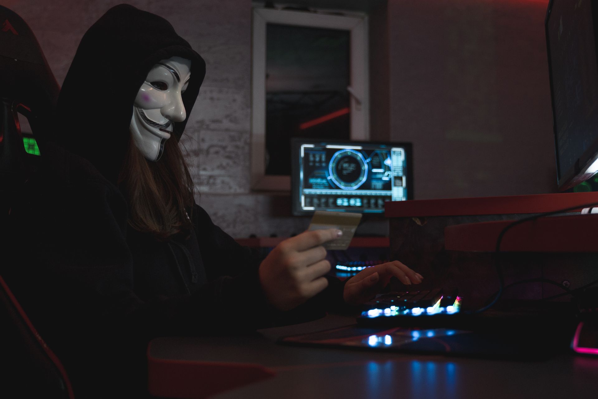 Masked hacker with credit card at computer, symbolizing cybercrime and anonymity